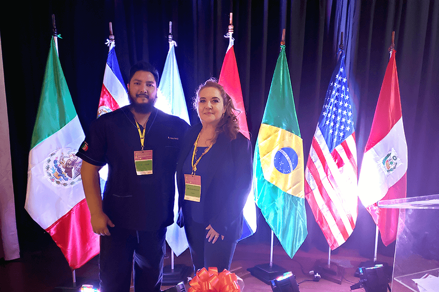 Dos miembros COINOTER con gafetes frente a banderas de países latinoamericanos participantes